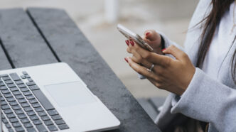 фото: жінка з телефоном за ноутбуком – мобільні додатки