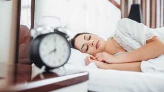 фото: жінка спить у ліжку, будильник – пізній сон і відпочинок