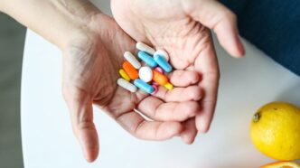 фото: вітаміни-пігулки у долоні і лимон на столі – дефіцит вітамінів