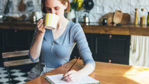фото: жінка пʼє каву і робить нотатки у фінансовому планері або щоденнику