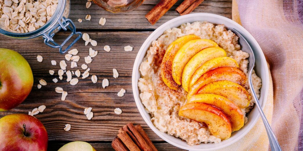 фото: Класична вівсянка з яблуком і корицею – тарілка гарячої каші з нарізаним яблуком, посипана корицею, на дерев’яному столі