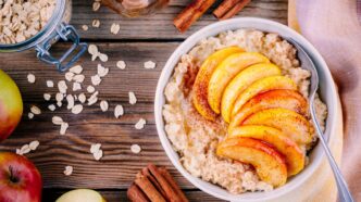 фото: Класична вівсянка з яблуком і корицею – тарілка гарячої каші з нарізаним яблуком, посипана корицею, на дерев’яному столі